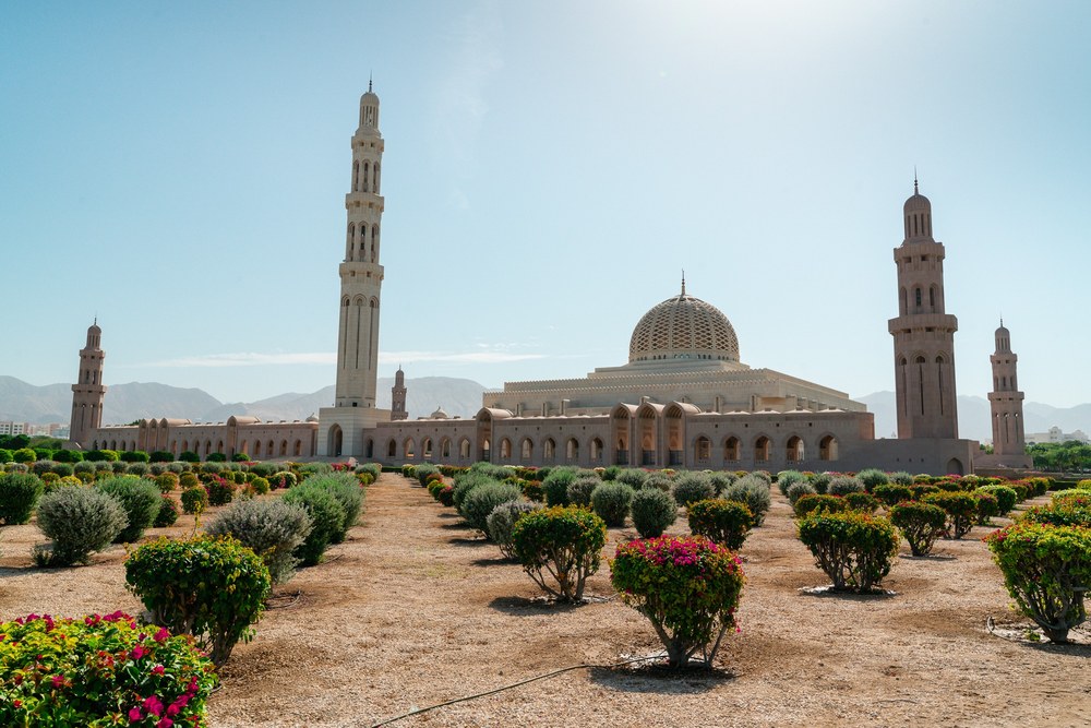 The dome and minarets of Sultan Qaboos Grand Mosque rise beyond gardens and flowering shrubs in Muscat, Oman.