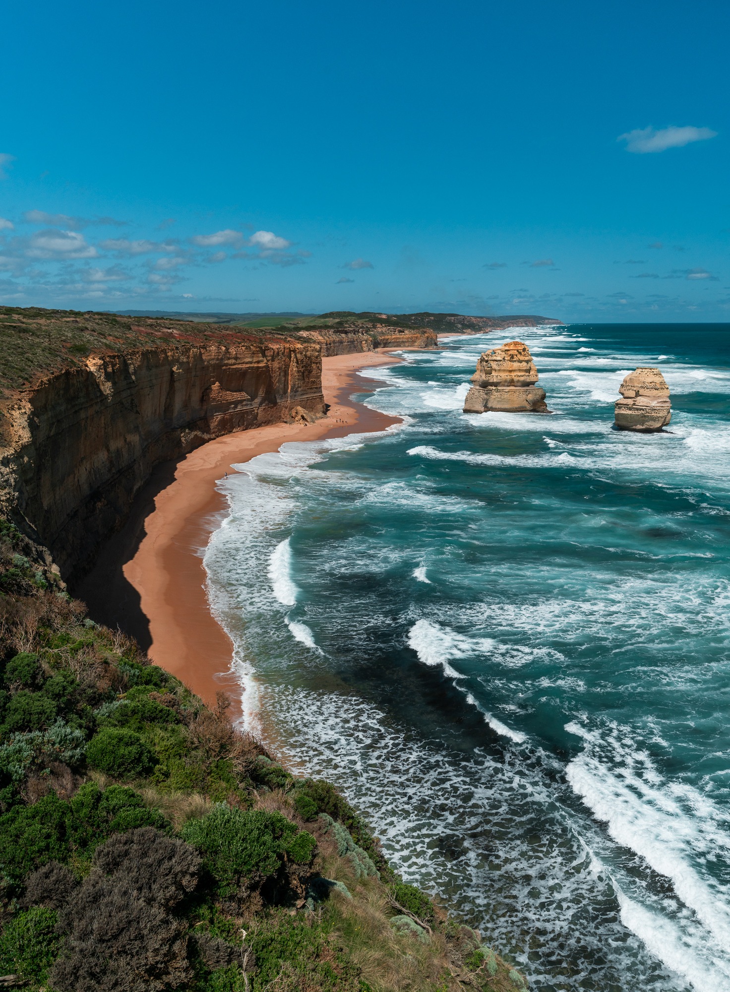 Waves roll toward the rugged coastline and limestone sea stacks of the Twelve Apostles, Australia.