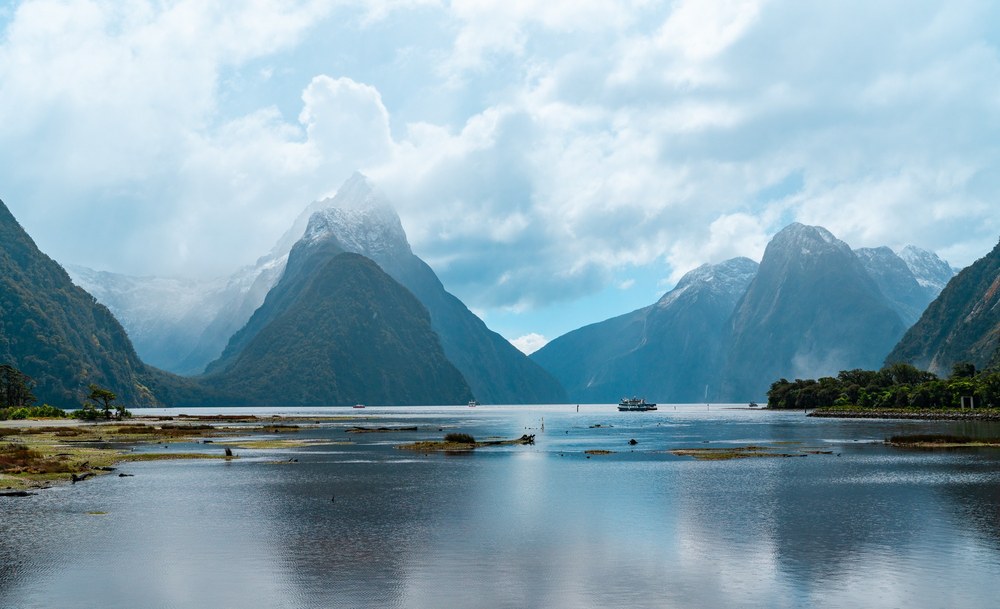 Cloud-wrapped mountains rise above the calm waters of Milford Sound, New Zealand.