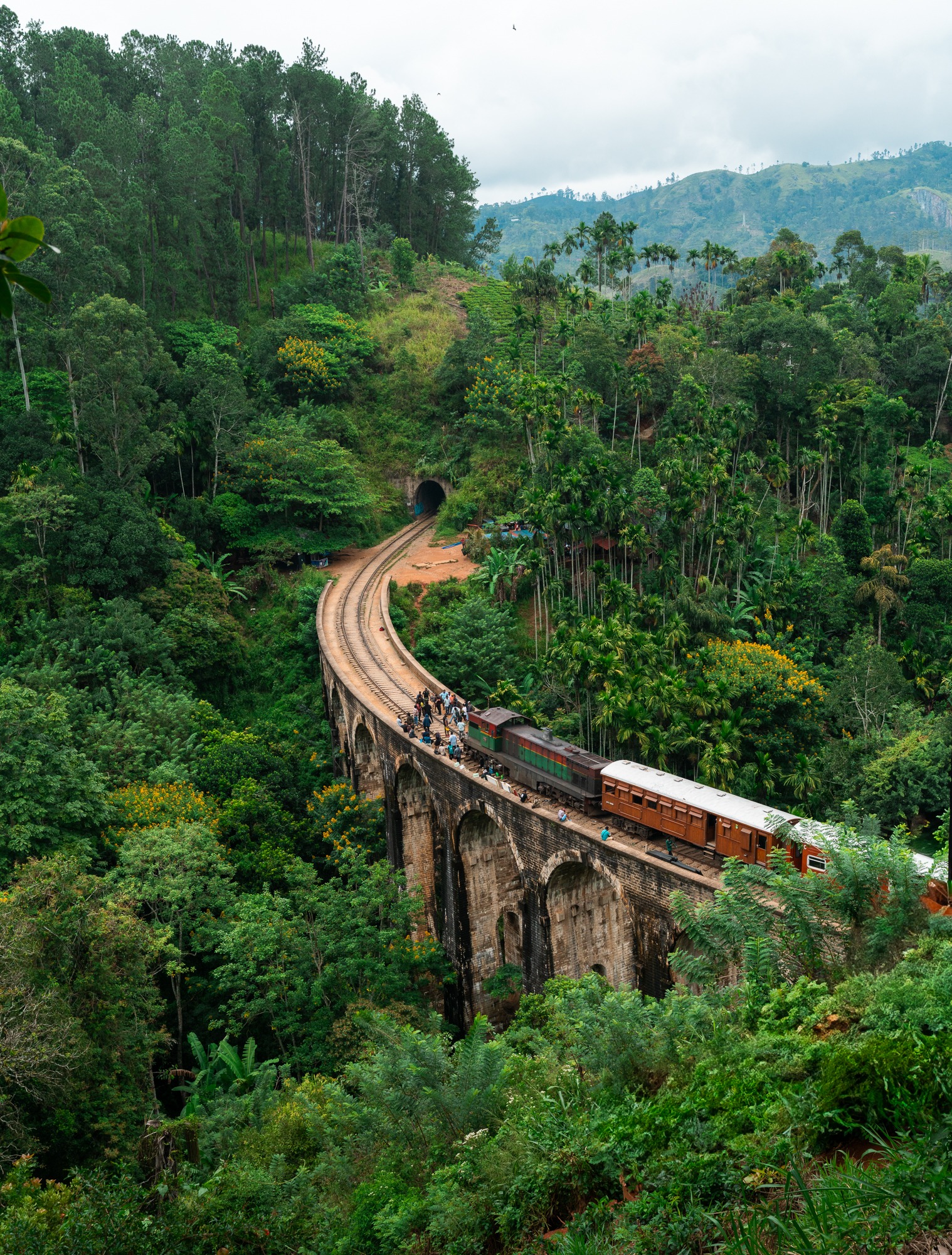 A train curves across the Nine Arch Bridge in Ella, Sri Lanka, surrounded by lush green hills.